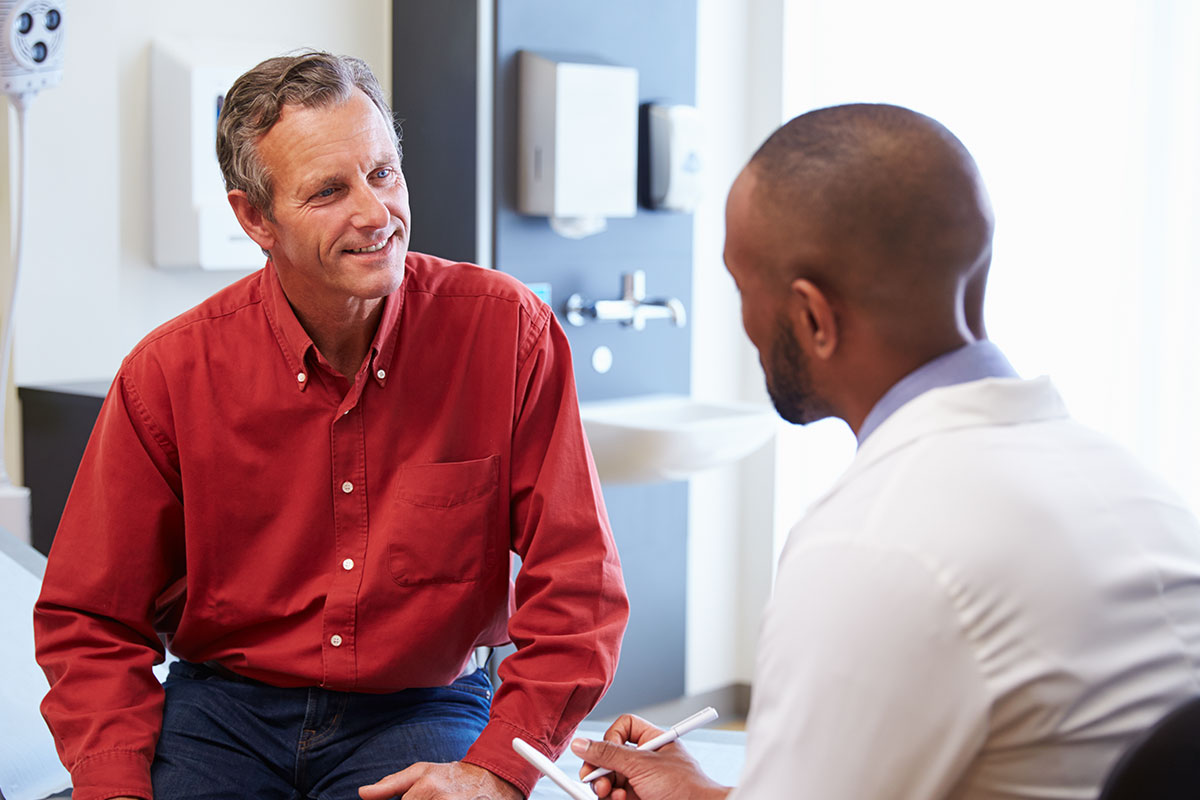 A male varicocele patient in a red shirt is interviewed by a Keck Medicine male infertility specialist in a medical setting