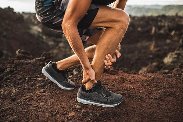 Someone in running shoes on a trail grabs their achilles tendon.