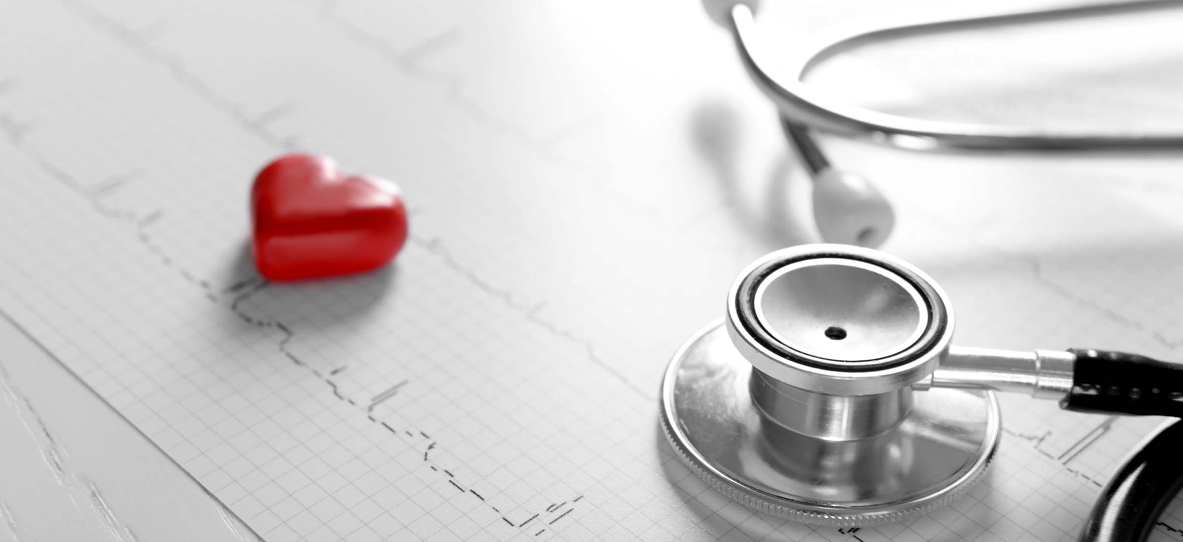 Stethoscope and red heart toy laying side by side on an electrocardiogram (ECG) chart.