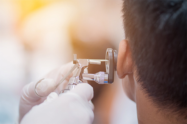 A doctor holds an instrument up to a patient's ear.