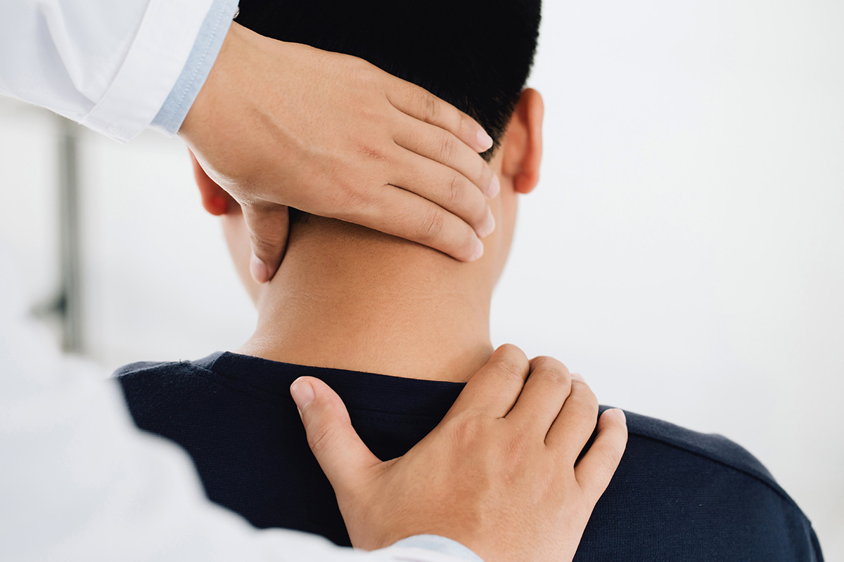 A Keck Medicine of USC physician examines the back of the neck of a young male patient with neck pain
