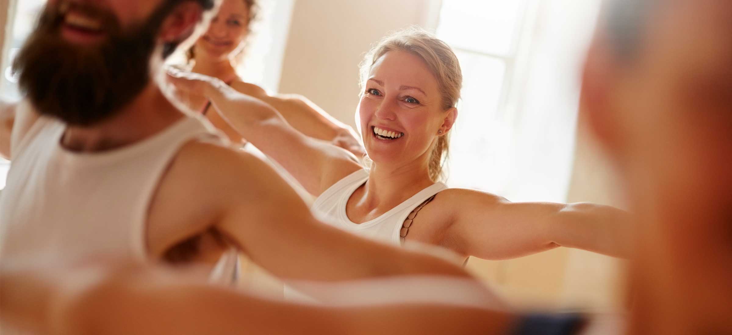 A woman smiles with her arms up in a yoga class.