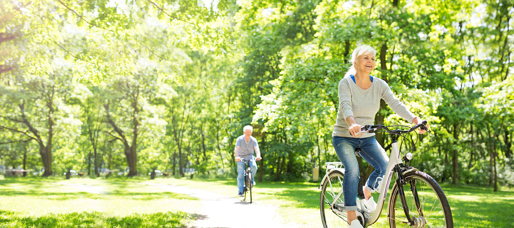 Older adult woman and older adult man riding their bikes in a park