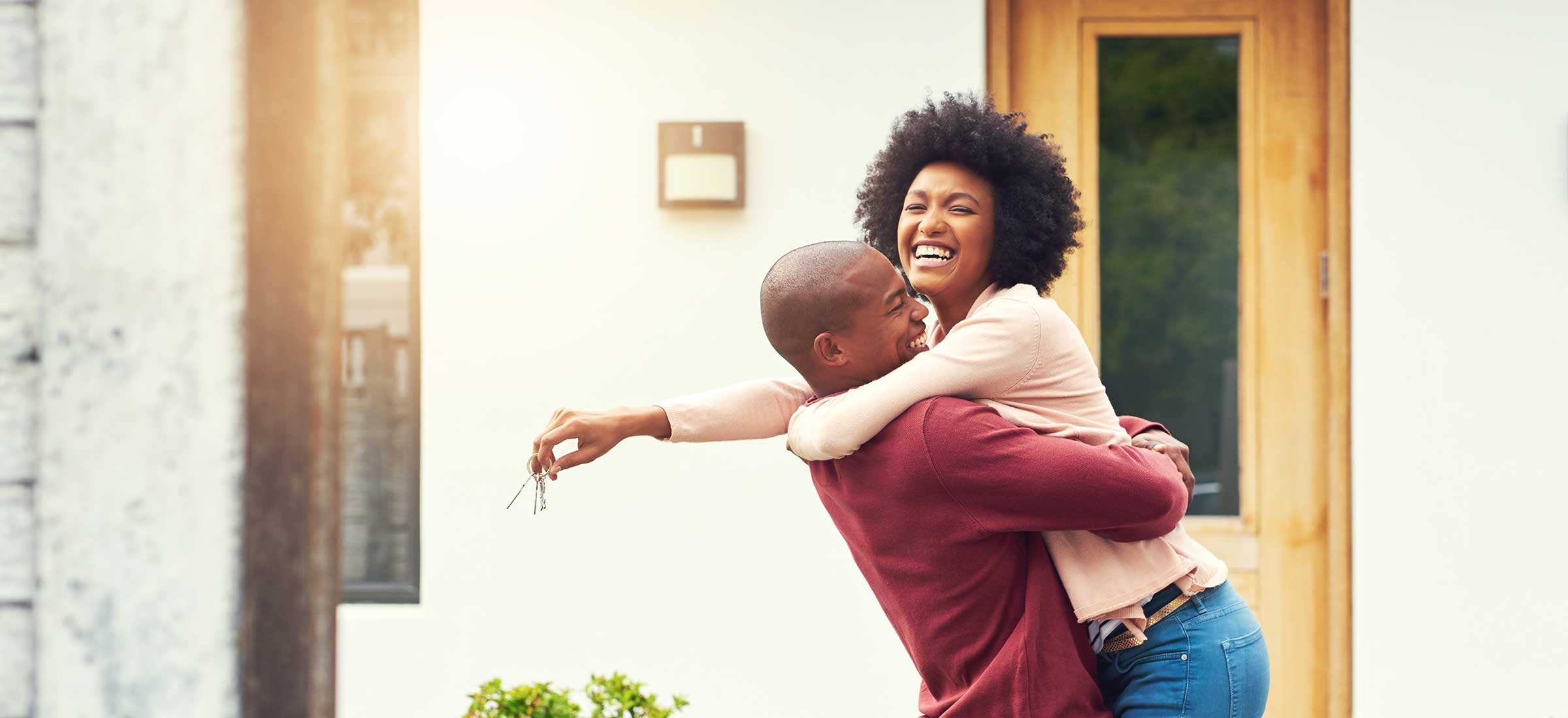 A smiling woman jumps into a man's arms with keys in her hand.