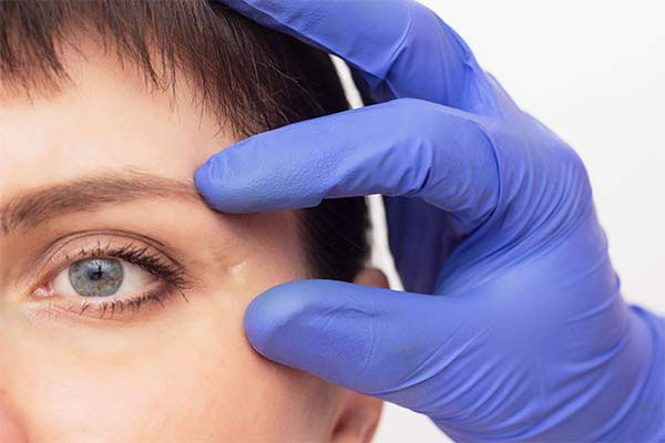A person with a scar near their eye is touched by a hand with a glove.