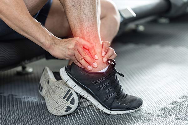 A man holds his ankle in pain with a red graphic over the ankle.