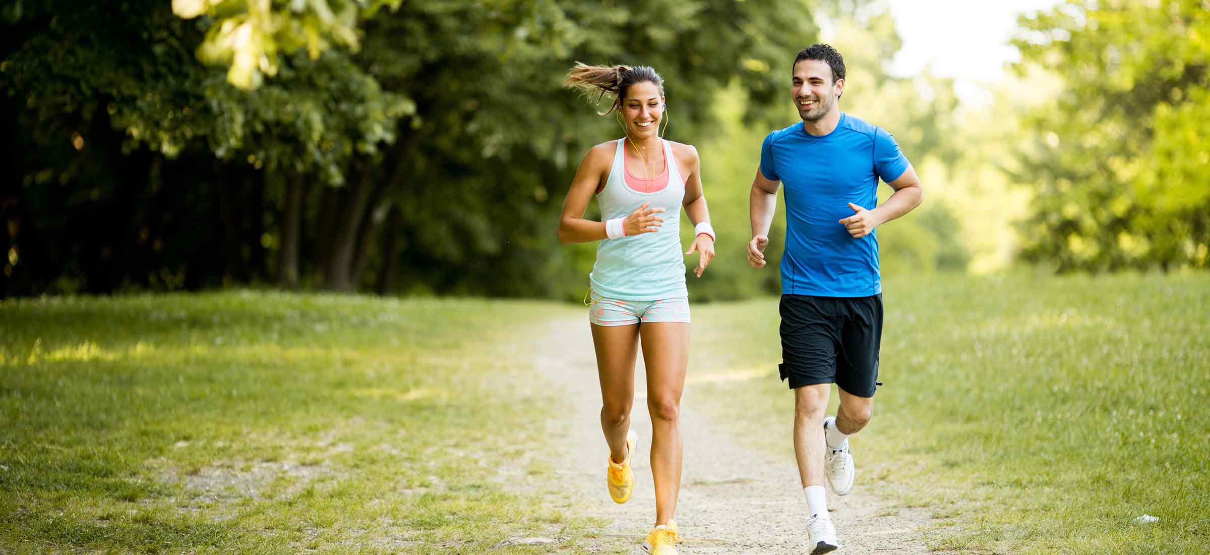 A young couple in shorts runs through the park.