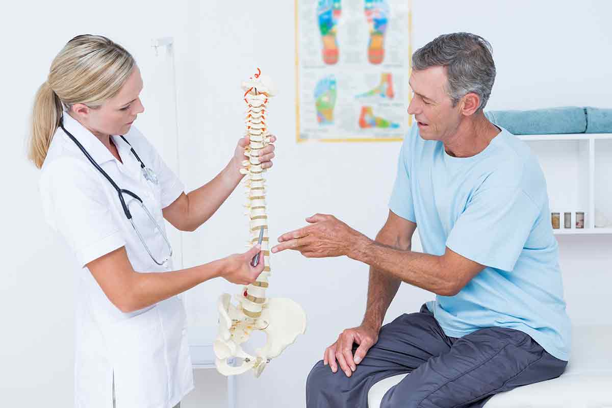 Doctor showing anatomical spine to her patient in medical office.