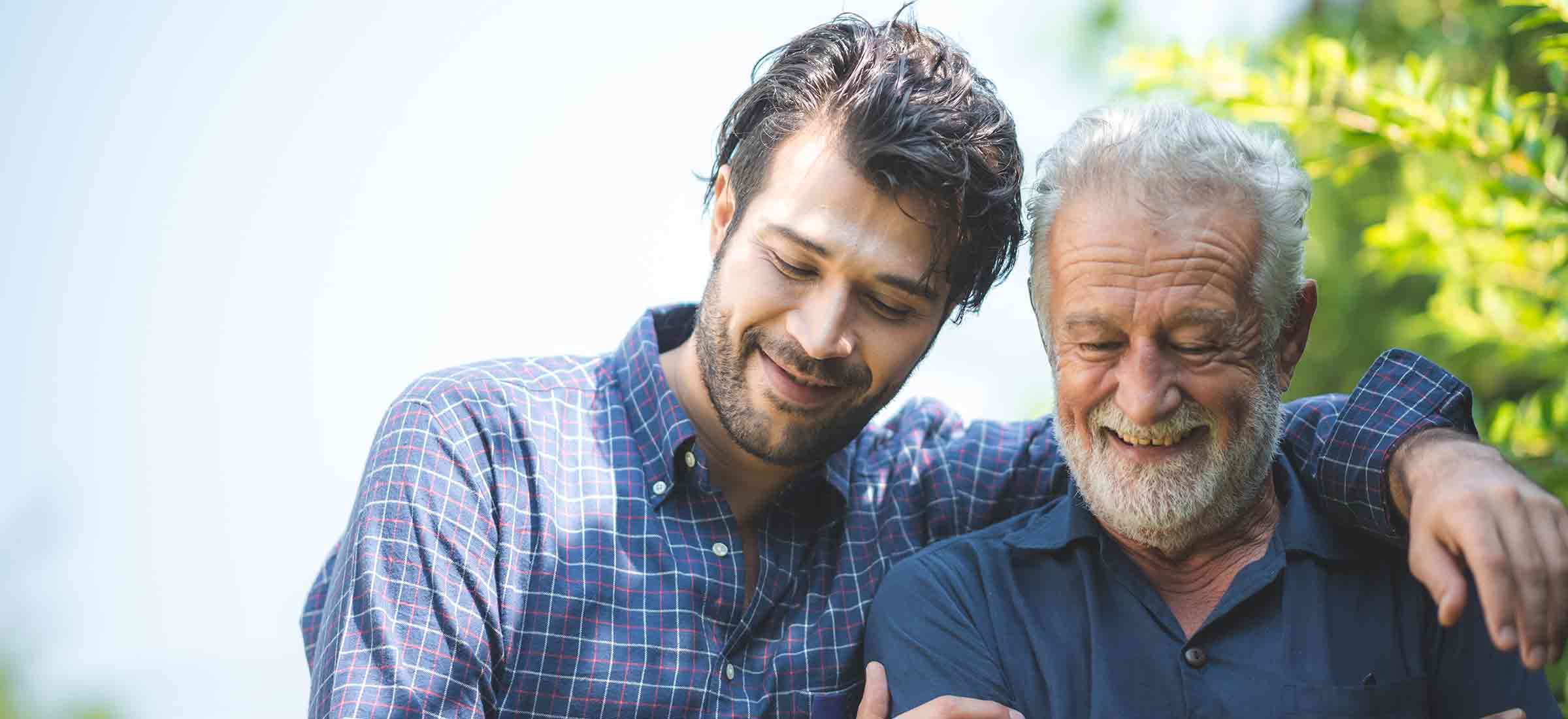 A young man puts his arm around an elderly man.