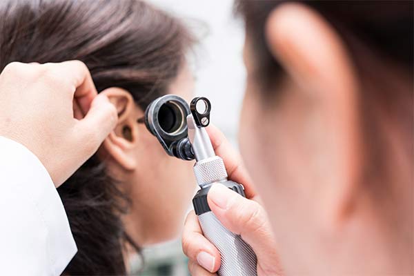 A doctor holds an instrument up to a patient's ear.