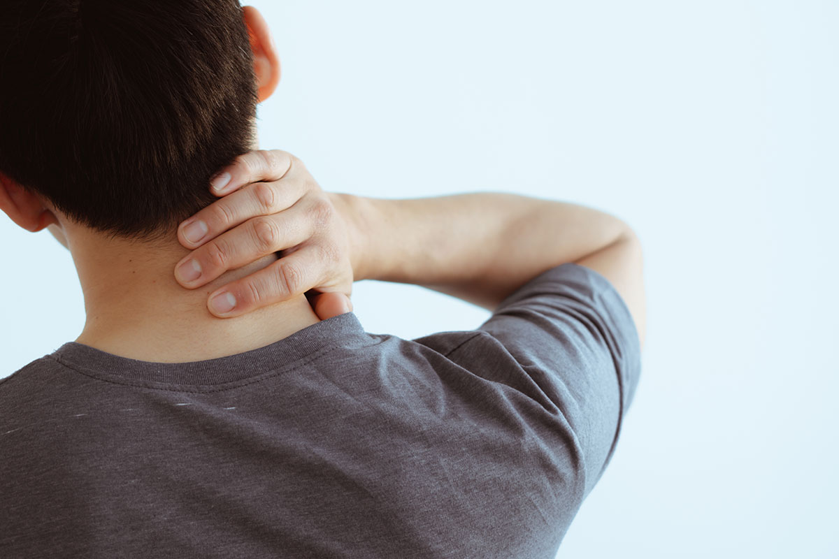 Close-up of man suffering from neck pain over gray background.