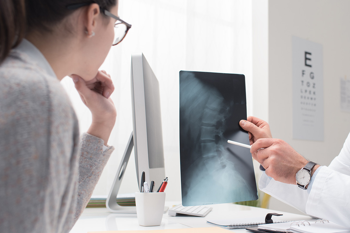A Keck Medicine neck degenerative disease specialist shows a young woman with glasses an X-ray of a herniated disk