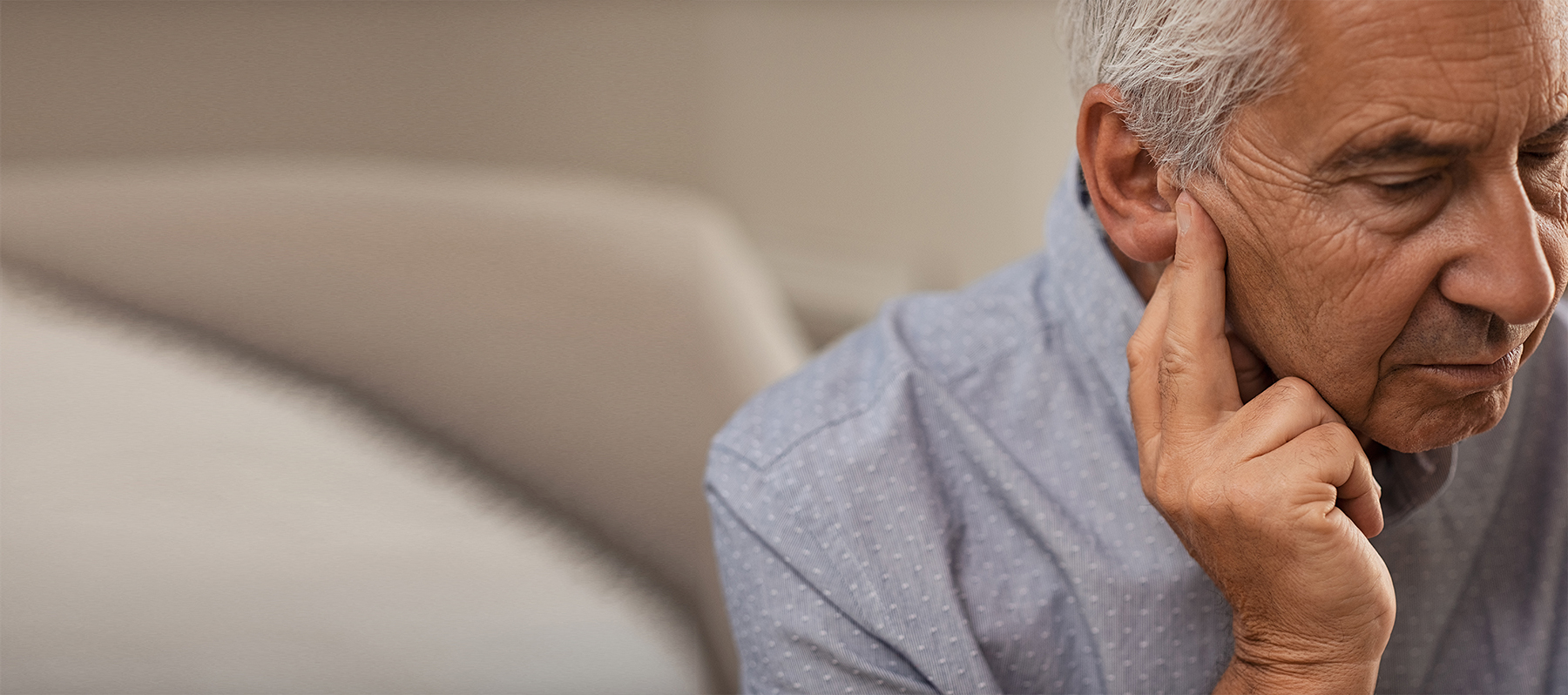 A senior man with hearing loss holds his right ear and considers ossiculoplasty treatment