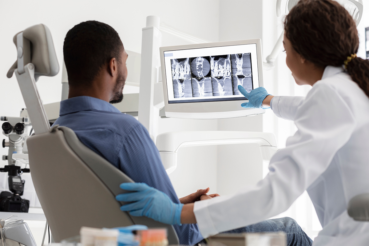 A male incontinence patient in a medical chair is shown pelvic floor X-rays by a female Keck Medicine urinary specialist