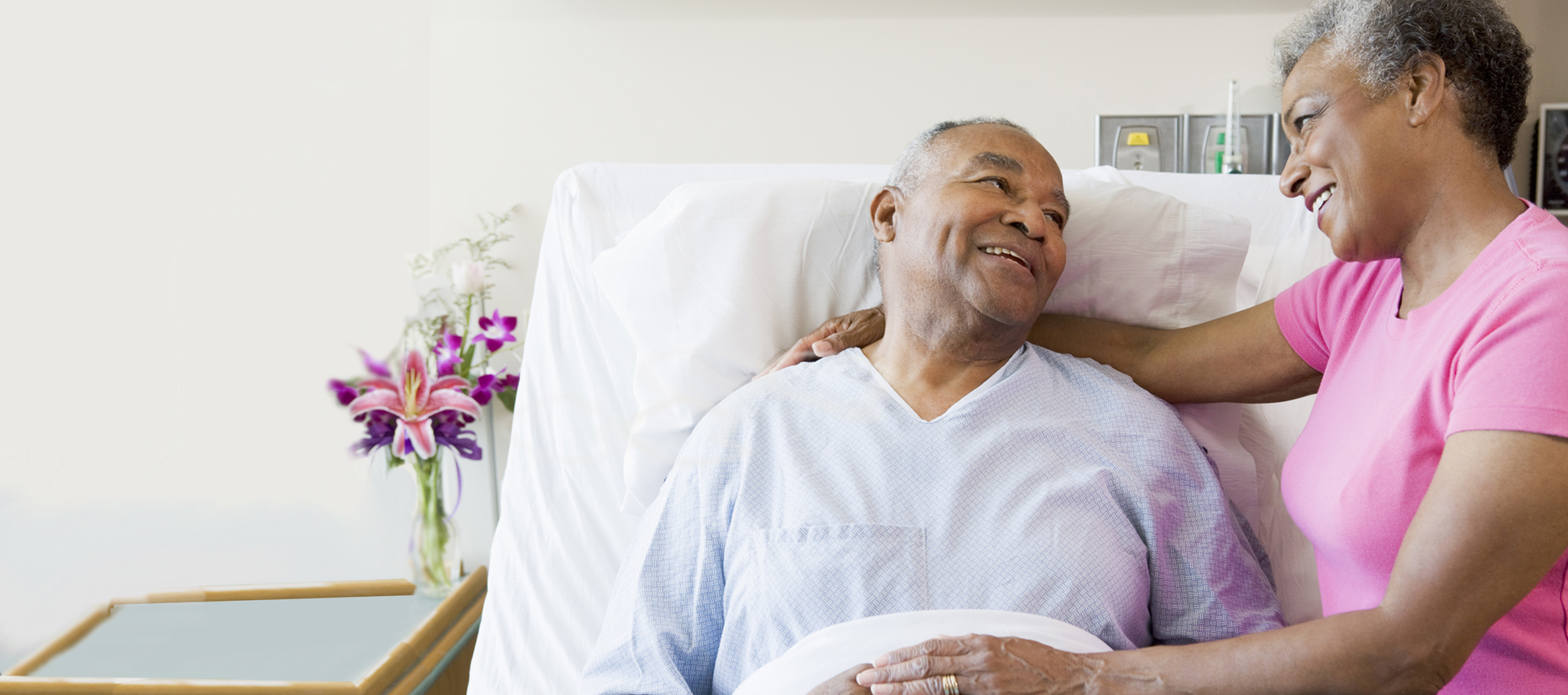 Female in pink puts her arms around a male liver transplant patient in a hospital bed