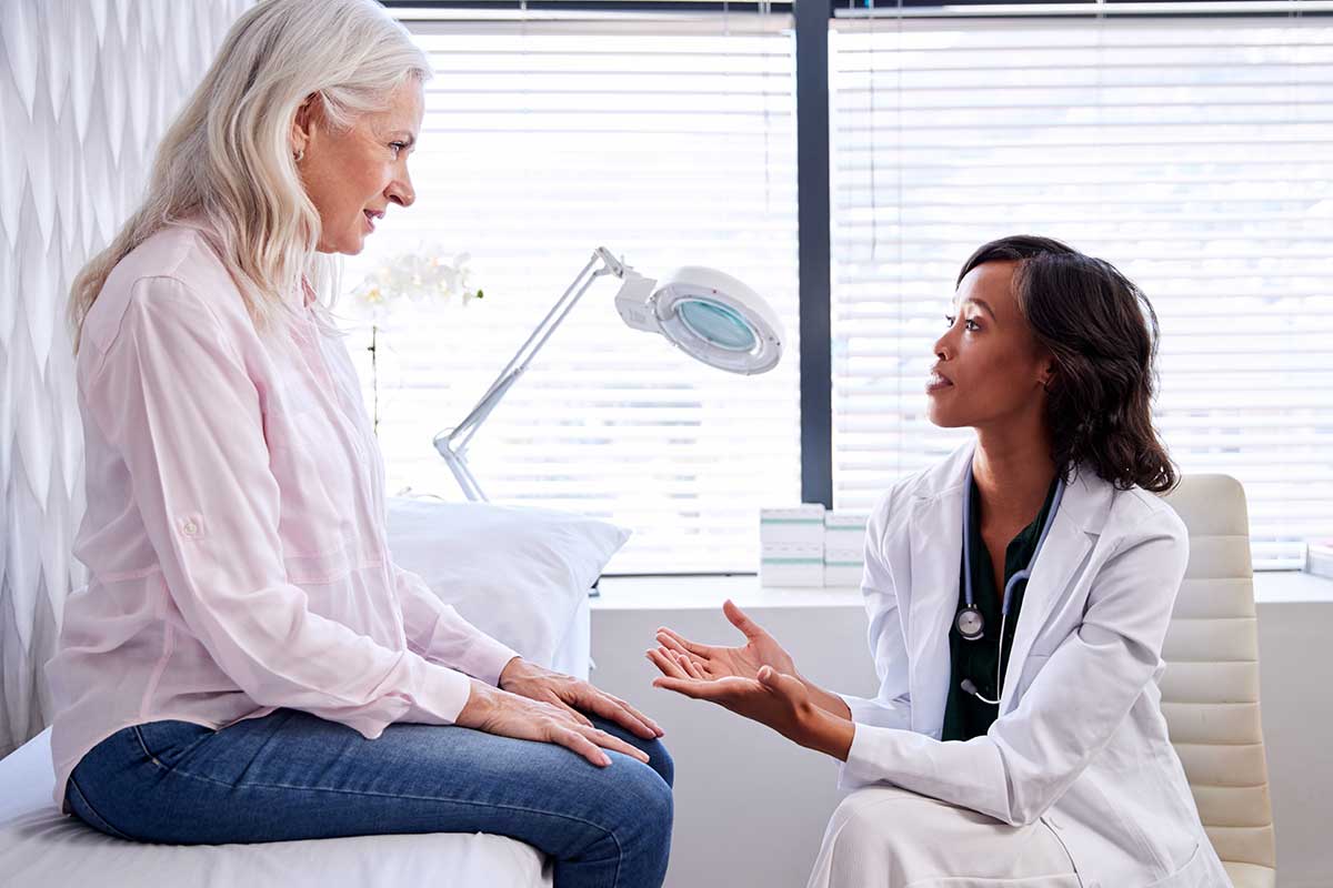 Mature woman in consultation with female doctor sitting on examination couch in office.