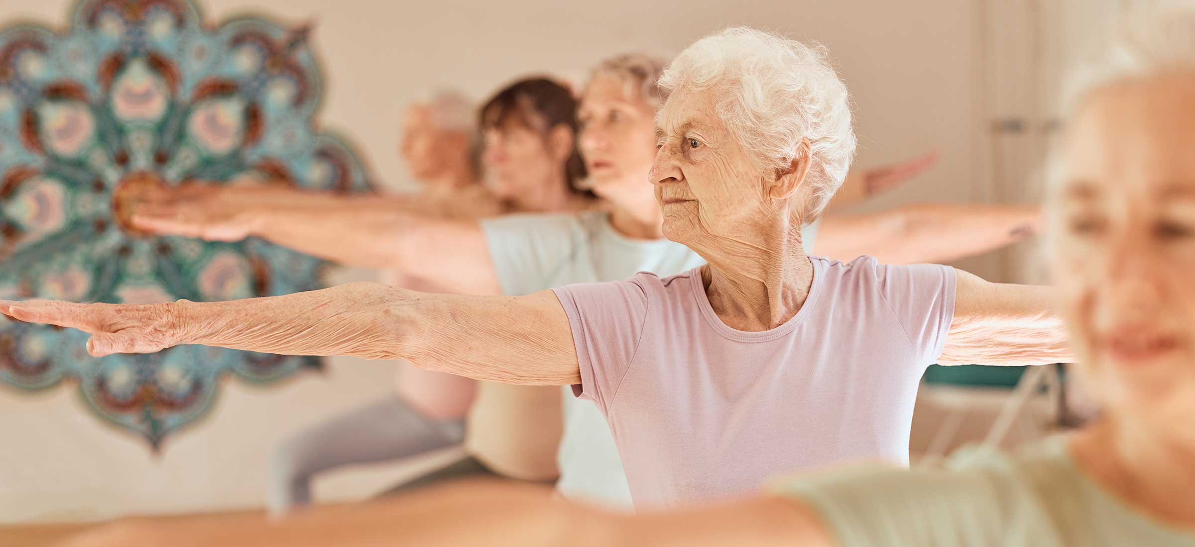 A group of elderly women hold their arms up in a yoga pose during a class.