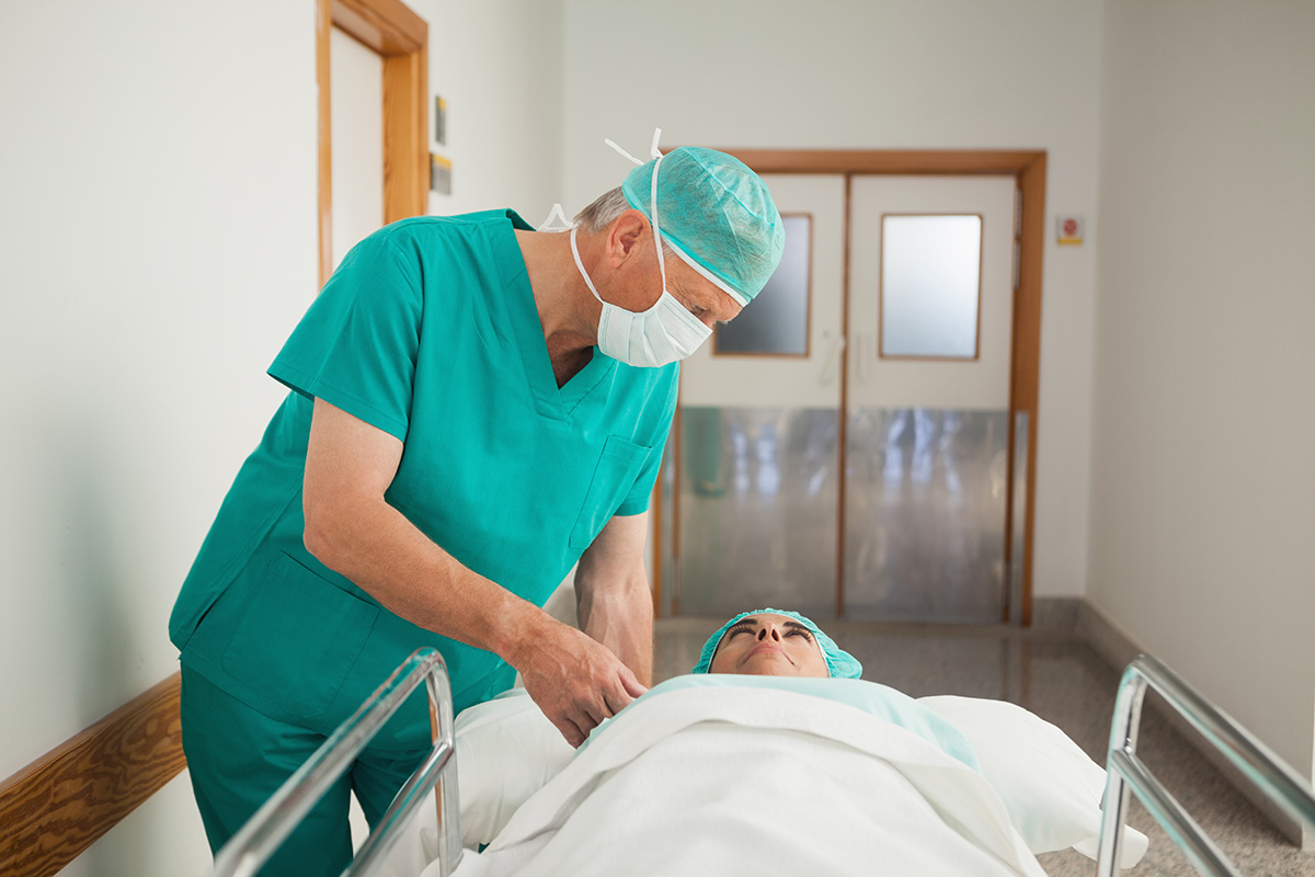 A male Keck Medicine blood cancer expert in green gear prepares a female patient on a gurney for a bone marrow transplant