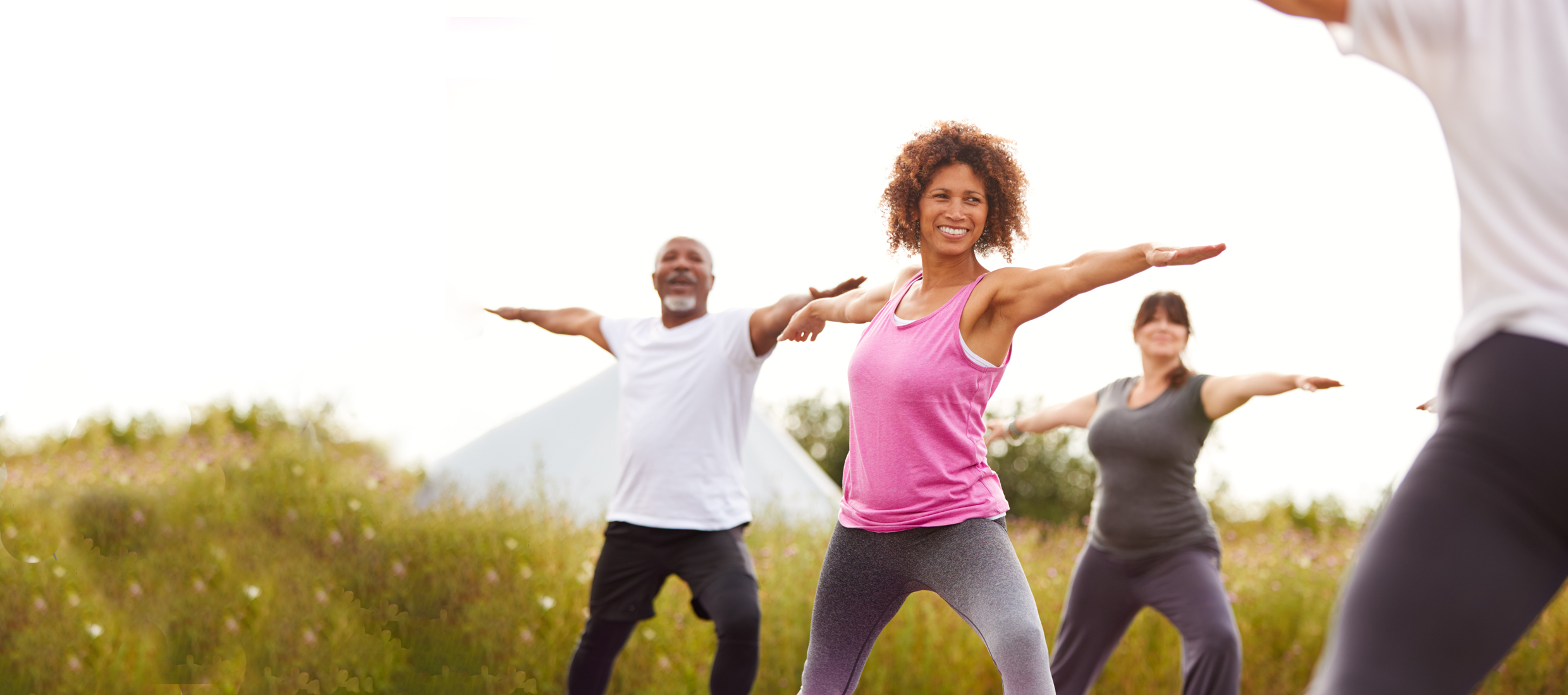 A young woman in a pink tank top, a man and another woman with vascular disease exercise with outstretched arms outdoors