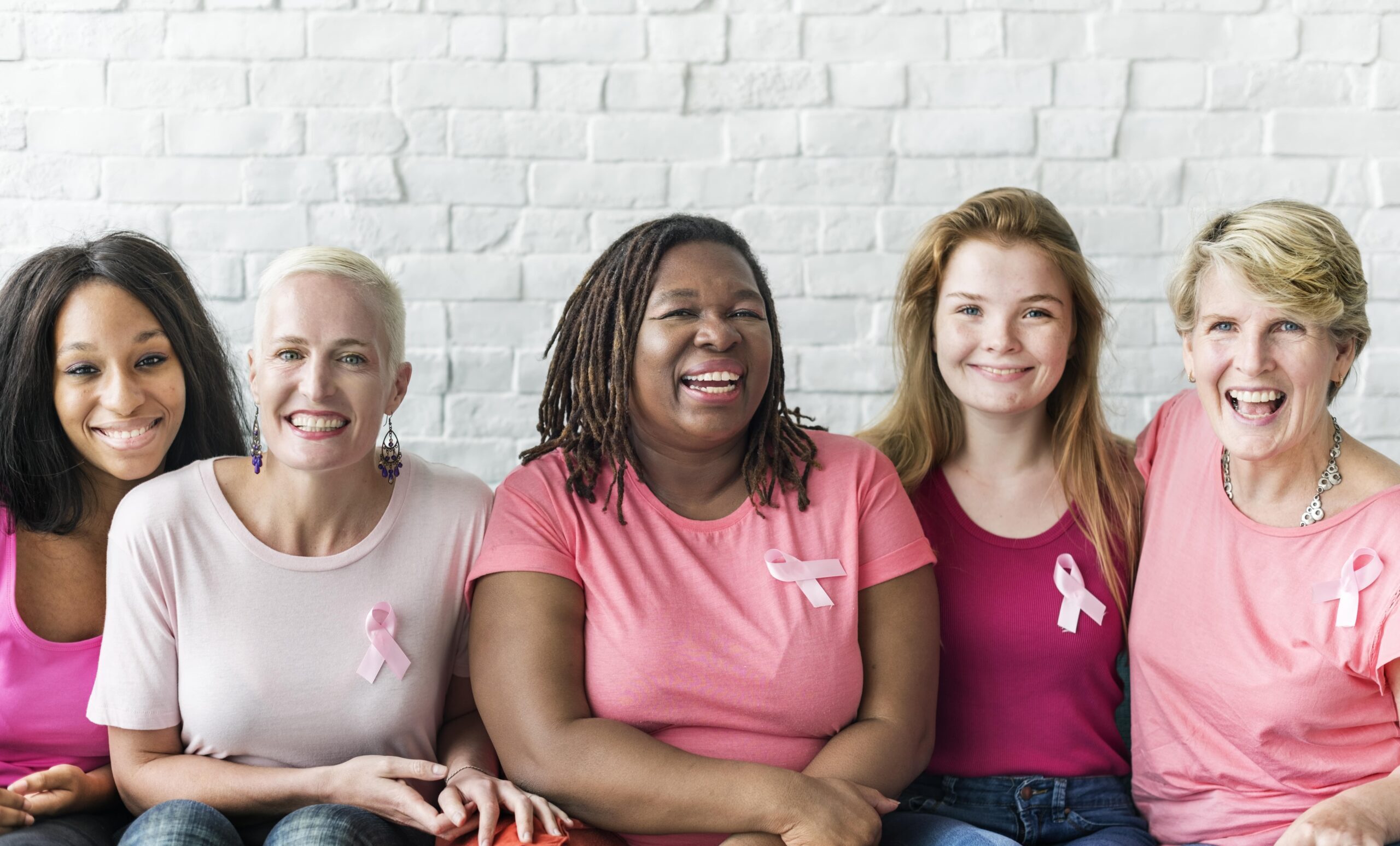 Five women smiling and wearing breast cancer awareness ribbons