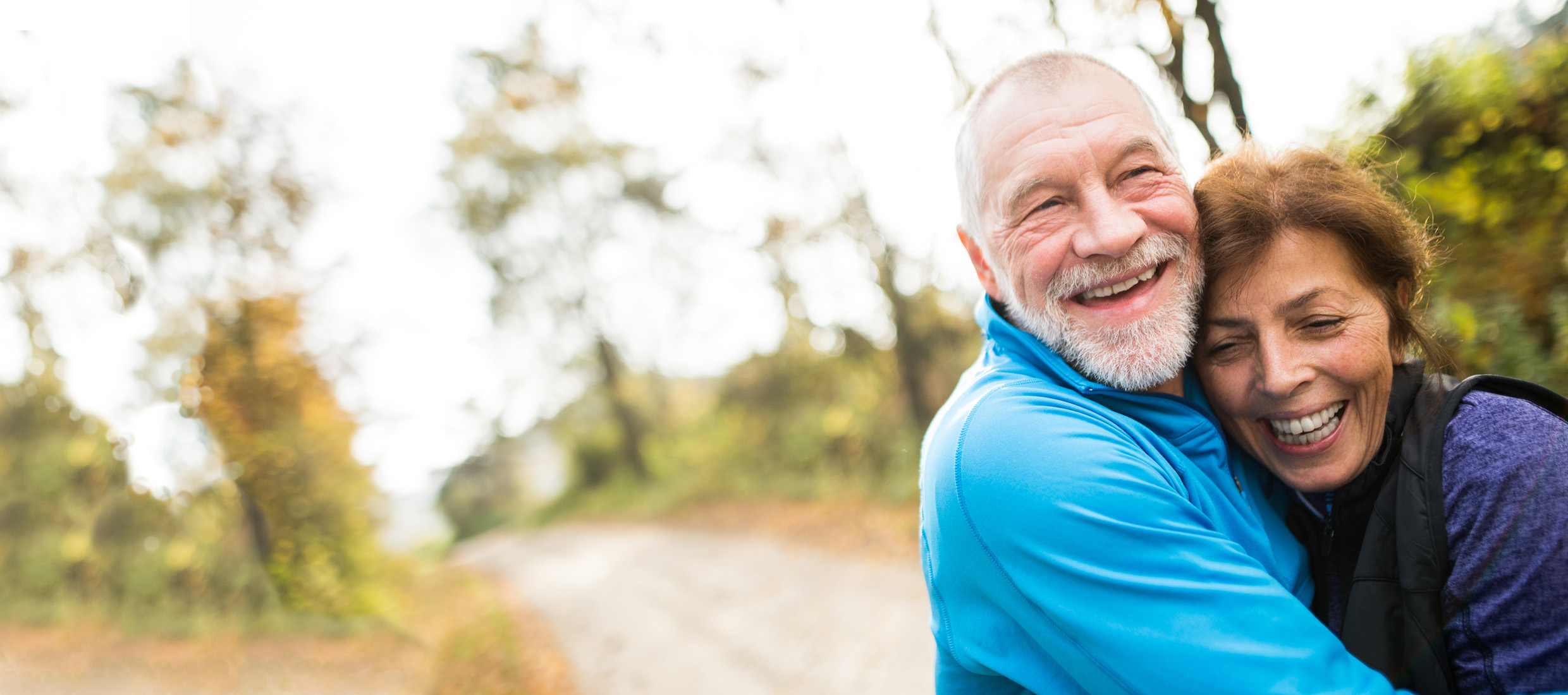 A man and a woman smiling and hugging while walking on a trail