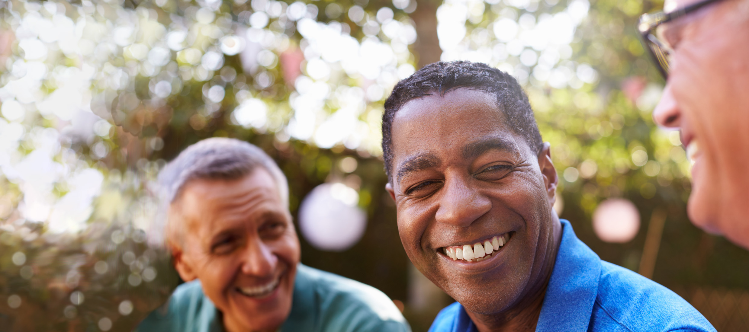 Three men smiling at one another while sitting in an outdoor space