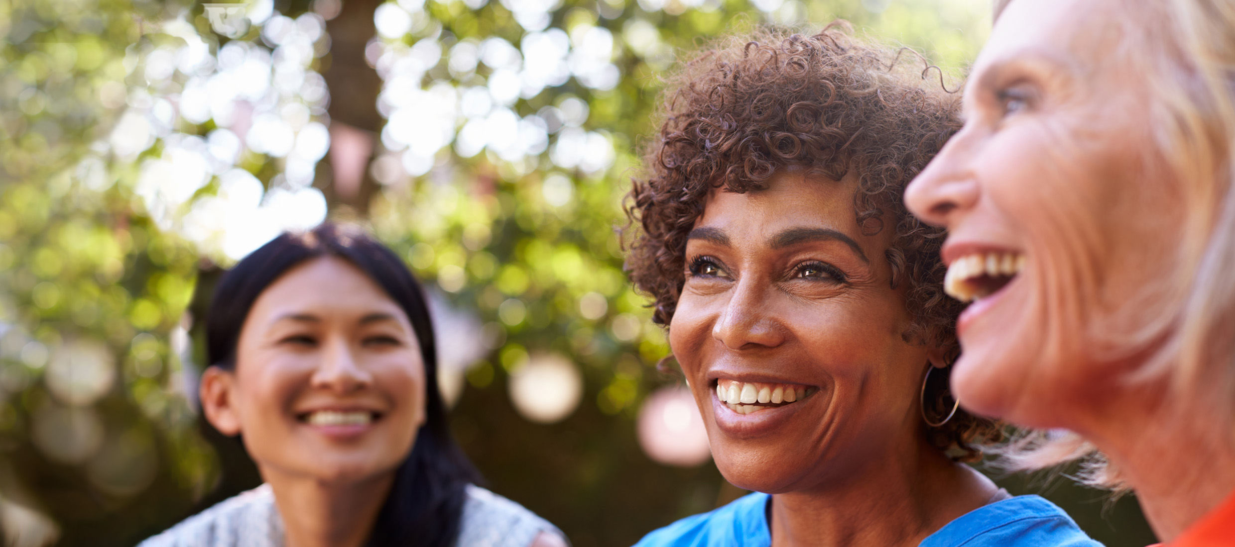 Three women smiling while outside in a park or backyard
