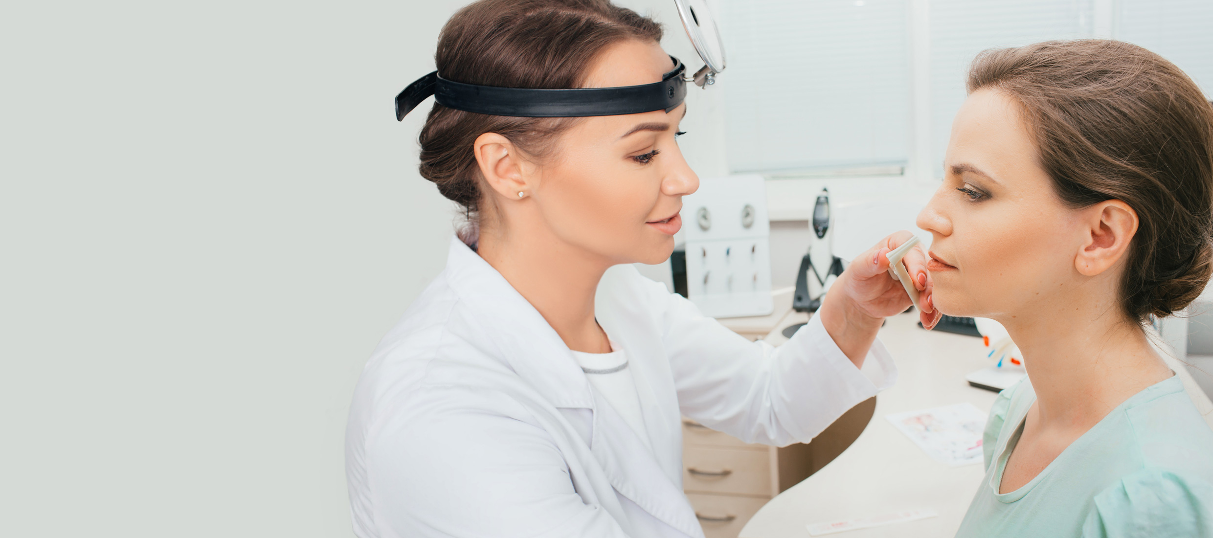 A female Keck Medicine sinus specialist wearing a head lamp treats a young female sinusitis patient in a medical setting