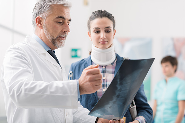 Doctor examining a young female patient's x-ray, she is wearing a cervical collar and has a serious neck injury.