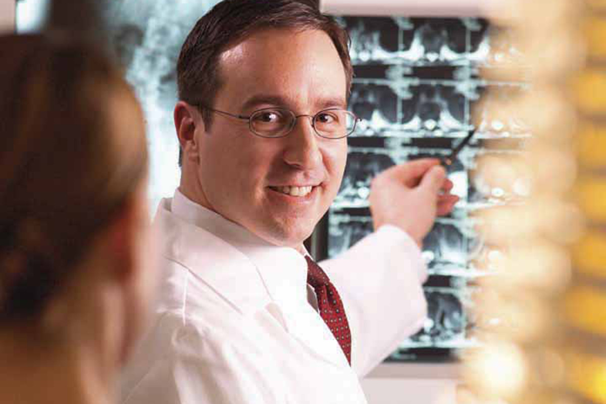 A Keck Medicine of USC spine surgeon wearing glasses smiles at a patient and shows him X-rays of his spinal fusion