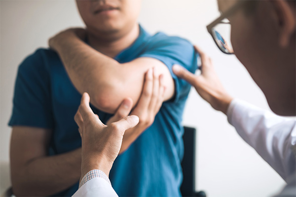 A doctor touches a patient's elbow as he sits in a medical office.