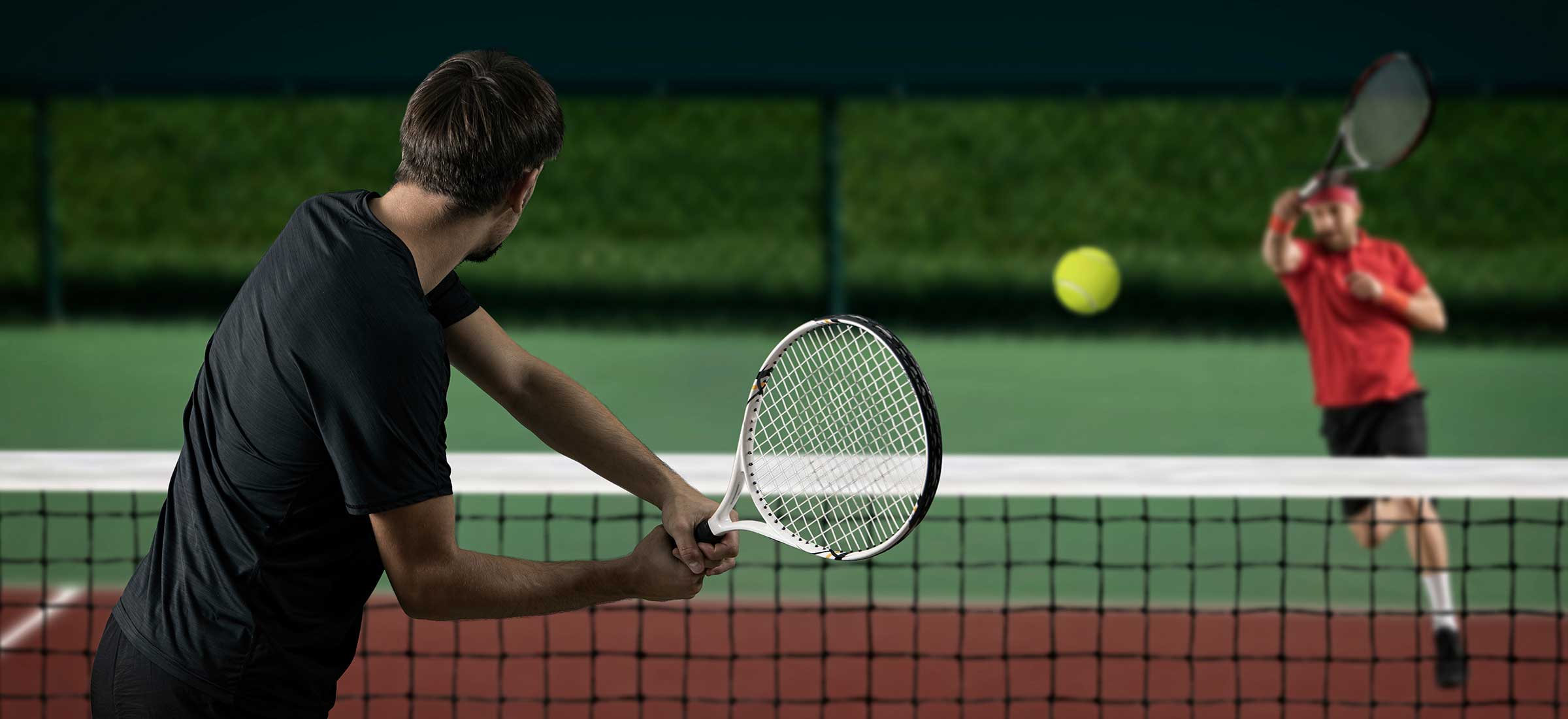 A tennis ball flies in the air between two male players.