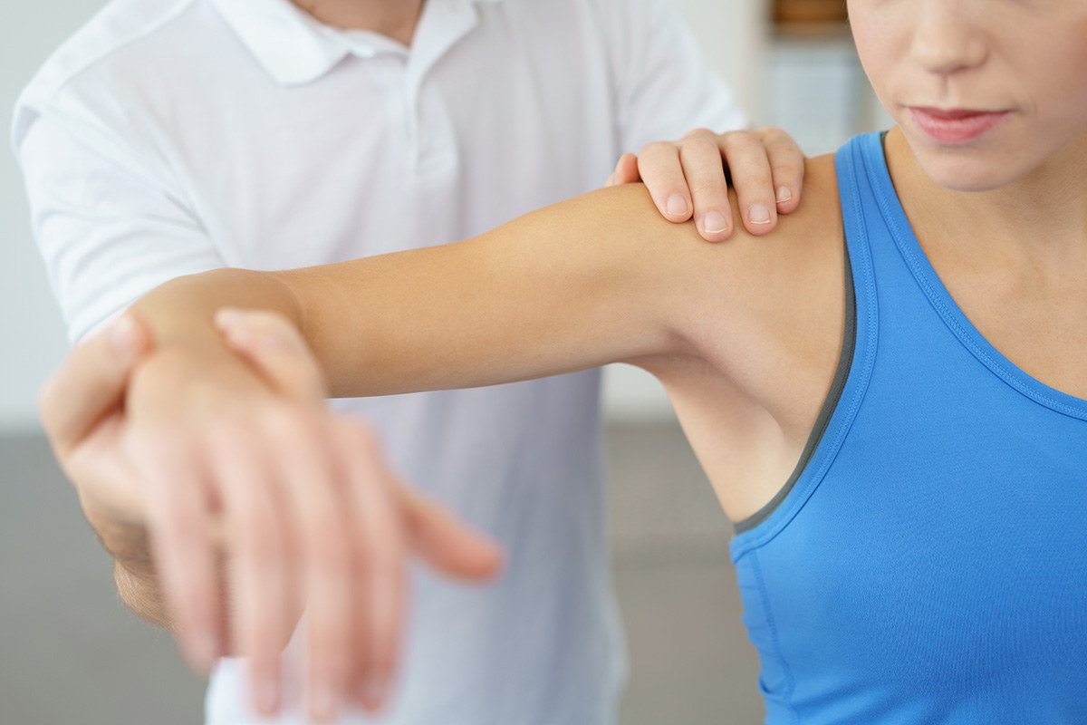 A man in a white shirt performs physical therapy on a female tennis elbow patient's bent right arm