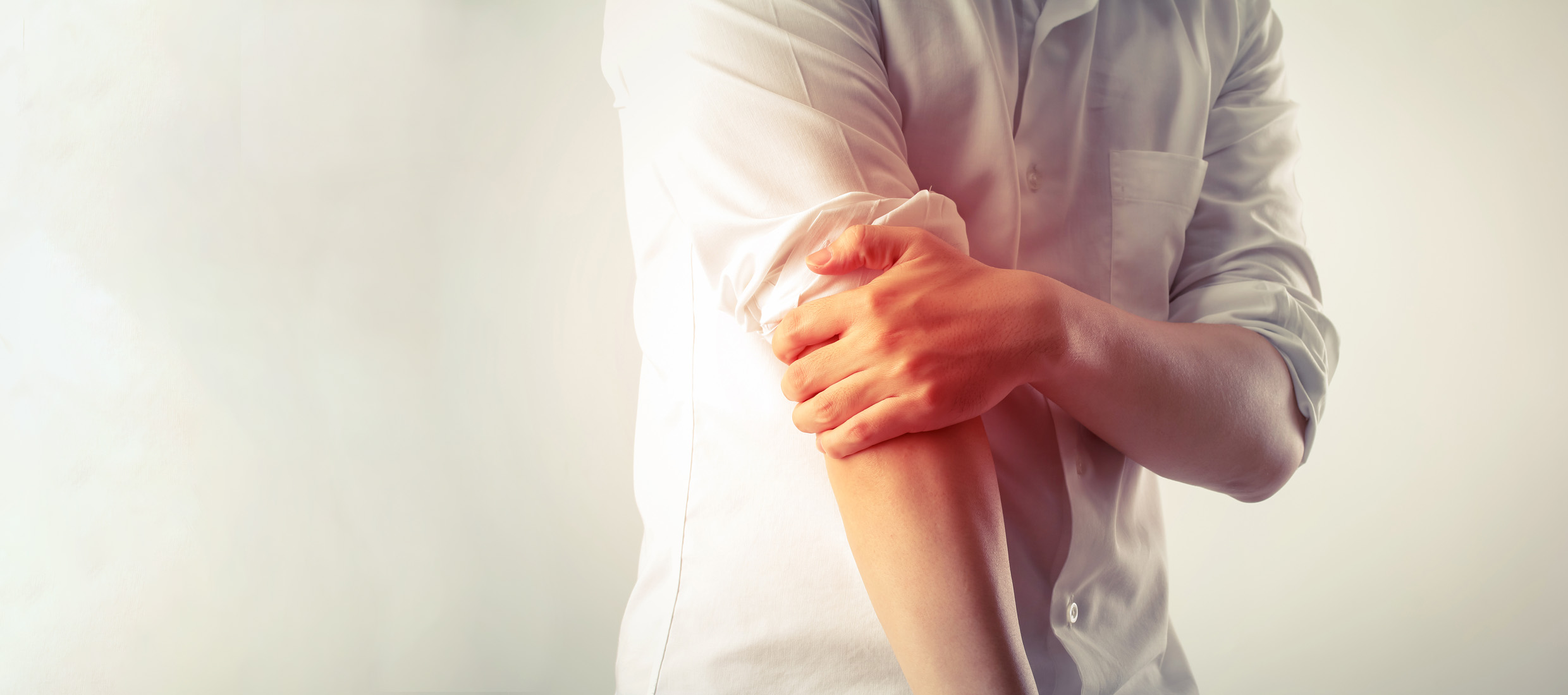 A young man with elbow pain from tennis elbow holds his right arm with his left hand