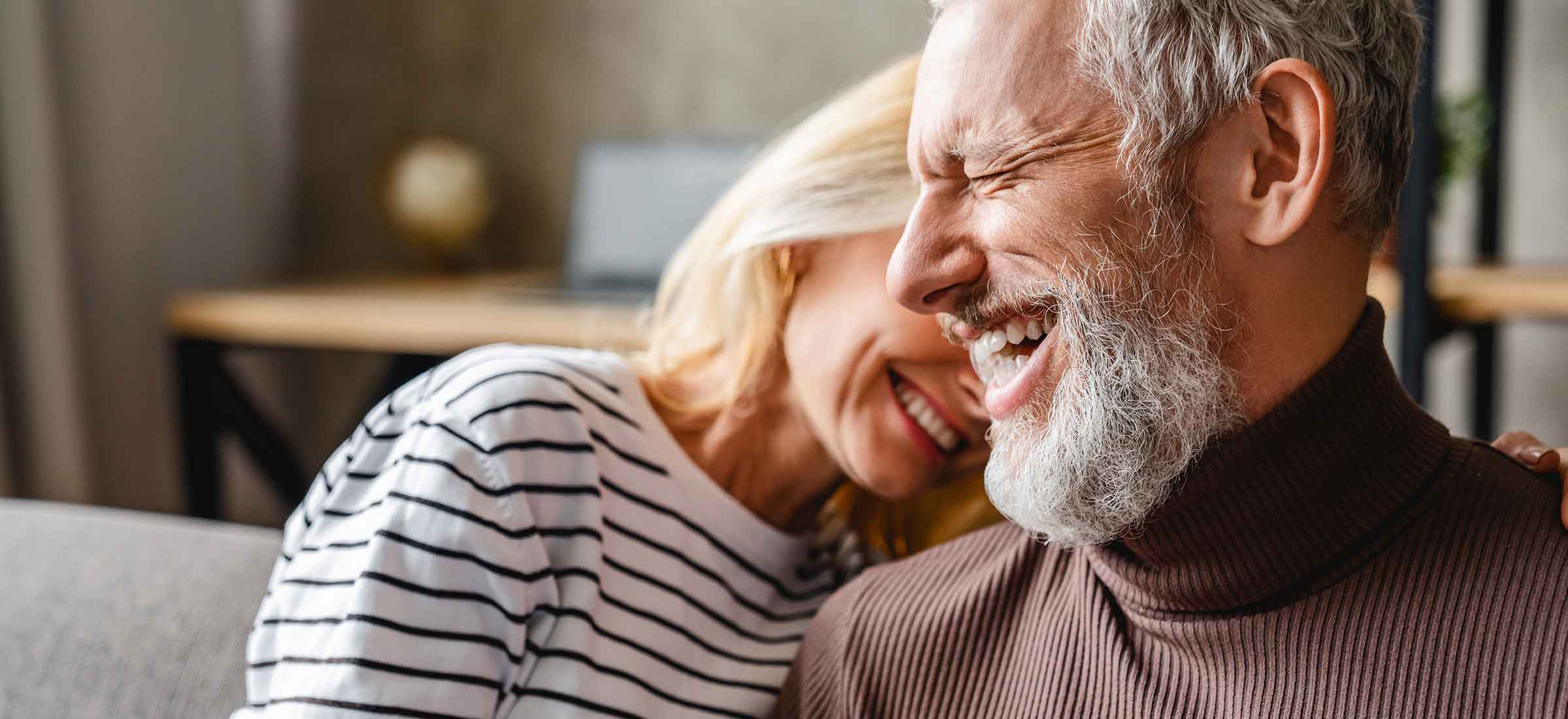 A man and woman smile while sitting on a couch.