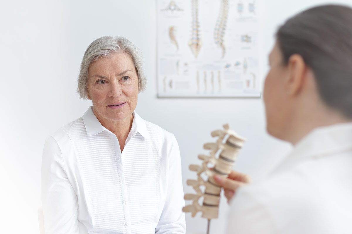 Doctor of rheumatolgy showing her senior patient a slipped disk on a backbone model.