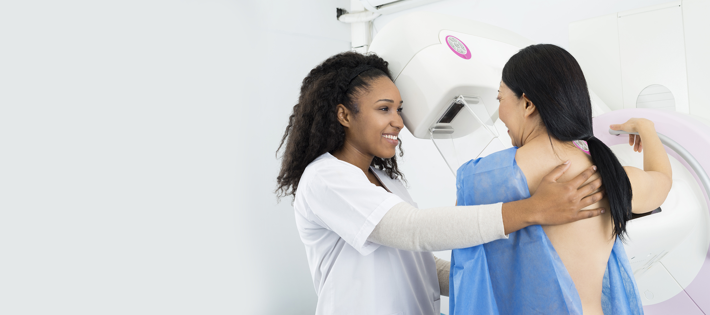 A female Keck Medicine doctor assists a female patient in a blue gown with a breast cancer screening at a mammogram machine
