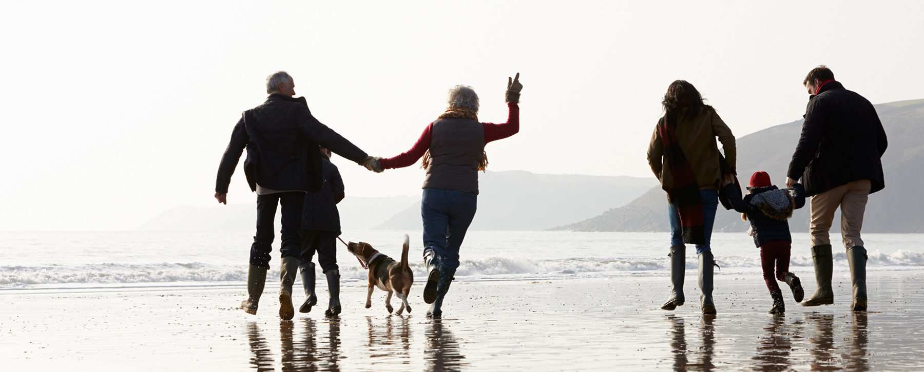 Two couples hold hands and spend family time with their children and a dog at the beach