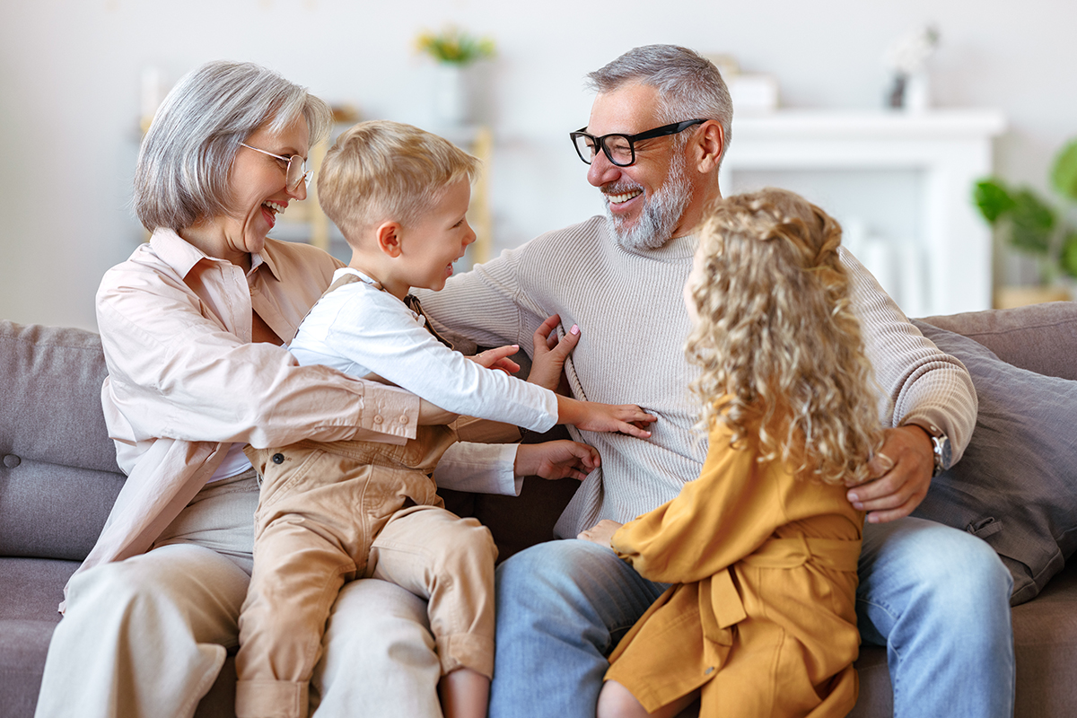 A male glaucoma patient wearing black eyeglasses smiles on a couch with his wife and two kids