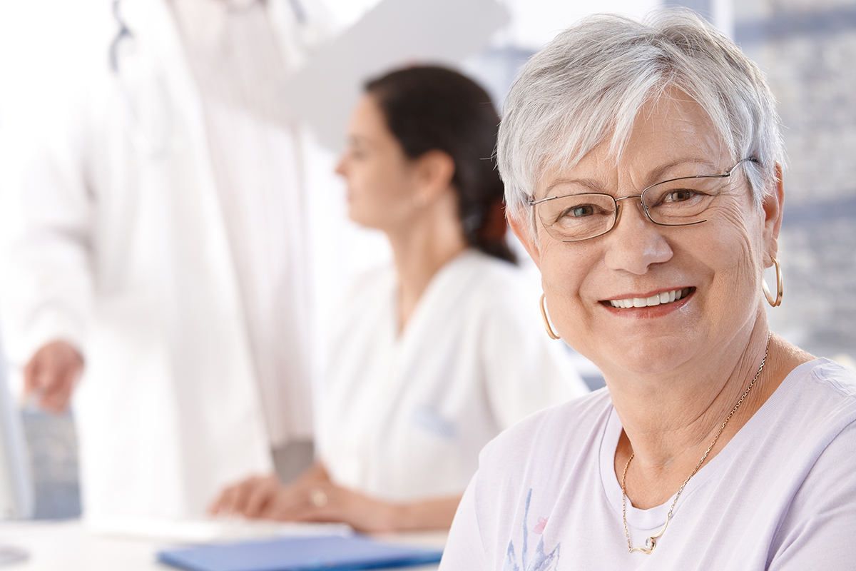 A female patient wearing eyeglasses is treated for eye infections and smiles in a medical office setting
