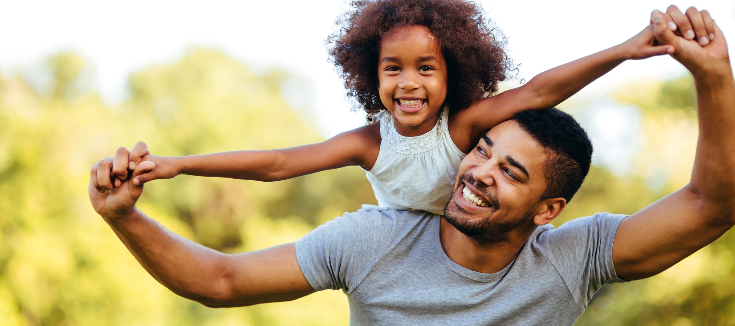 A young daughter with asthma on dad's right shoulder holds his hands with outstretched arms