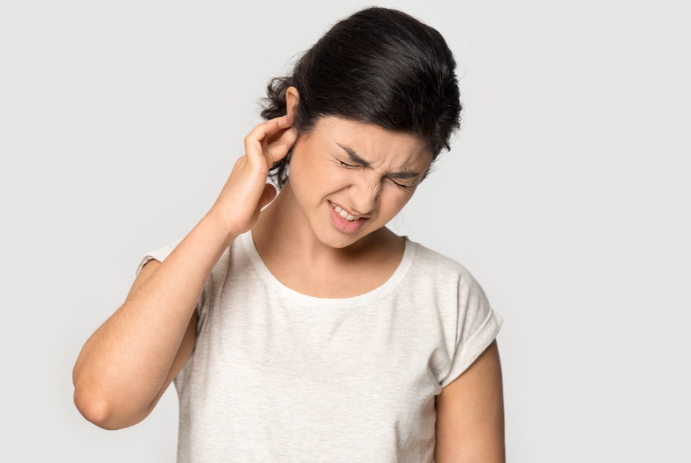 A young woman with impacted ear wax touches her painful ear