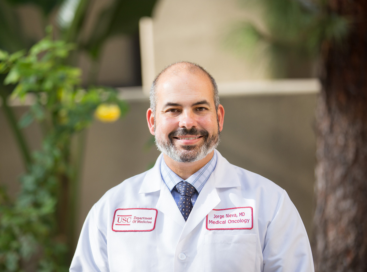 Jorge Nieva, a Keck Medicine medical oncologist who treats lung cancer, smiles by a brick wall and fruit trees