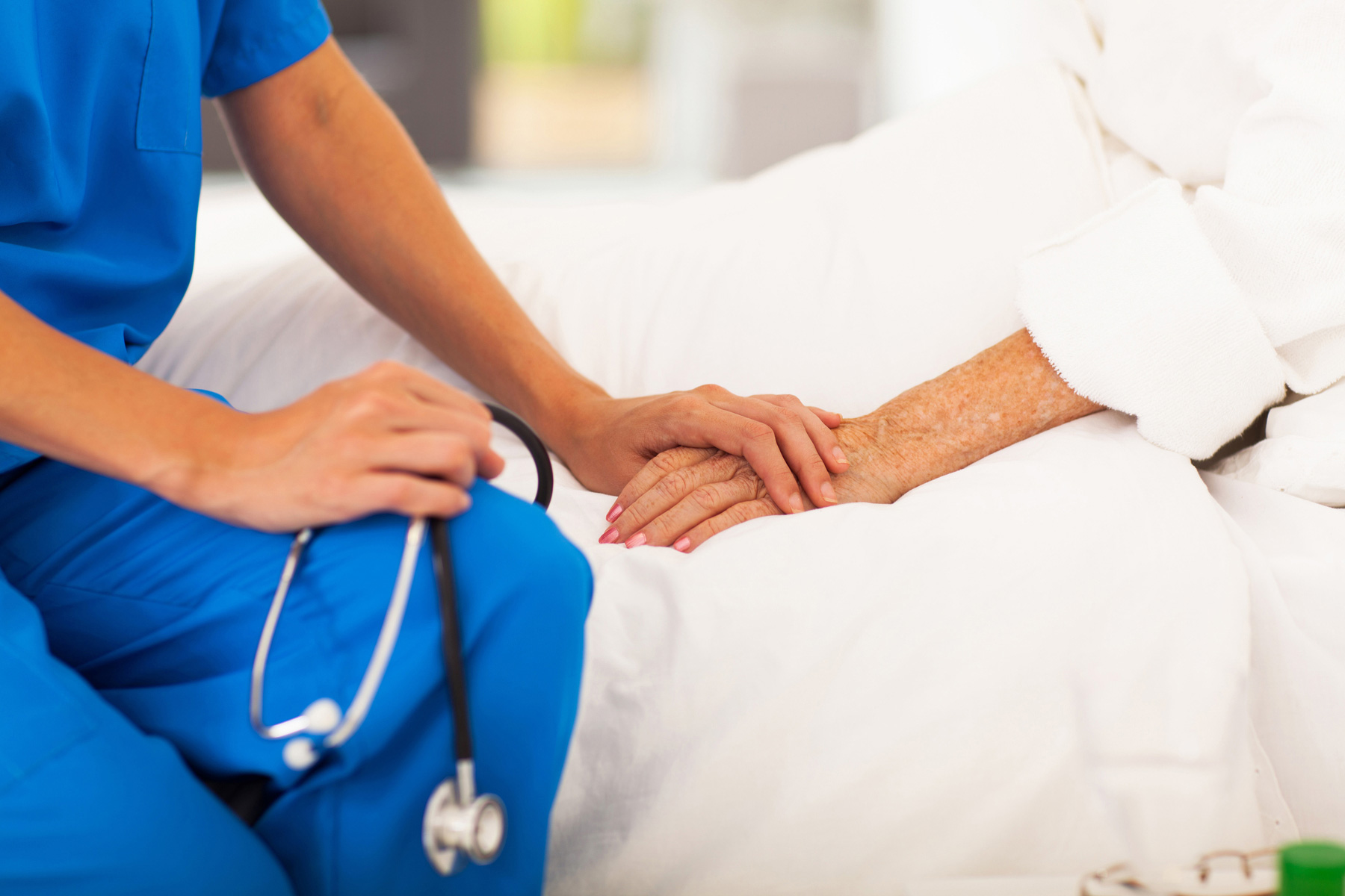 A female Keck Medicine lymphedema expert in blue holds a stethoscope and holds the hand of a senior woman who has swelling