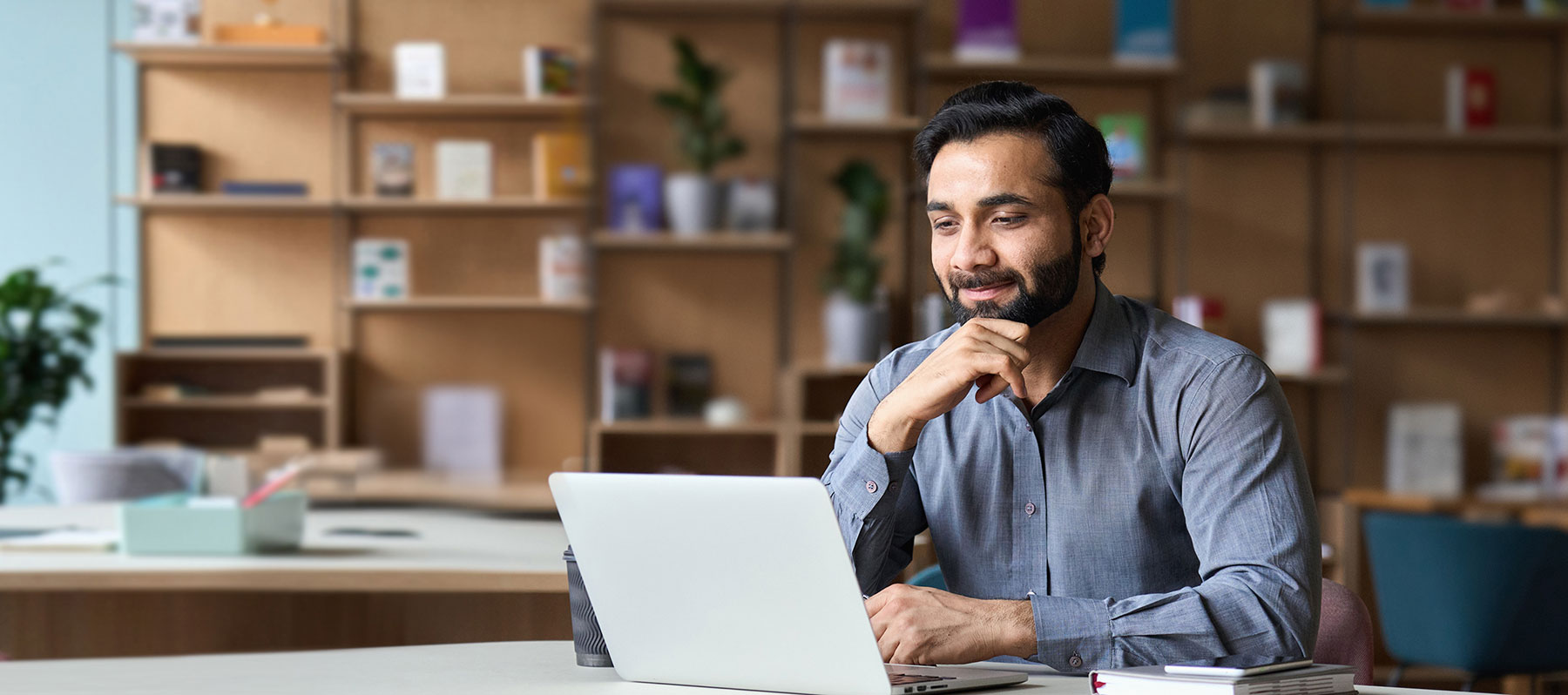 Smiling Indian businessman working on laptop in modern office lobby space