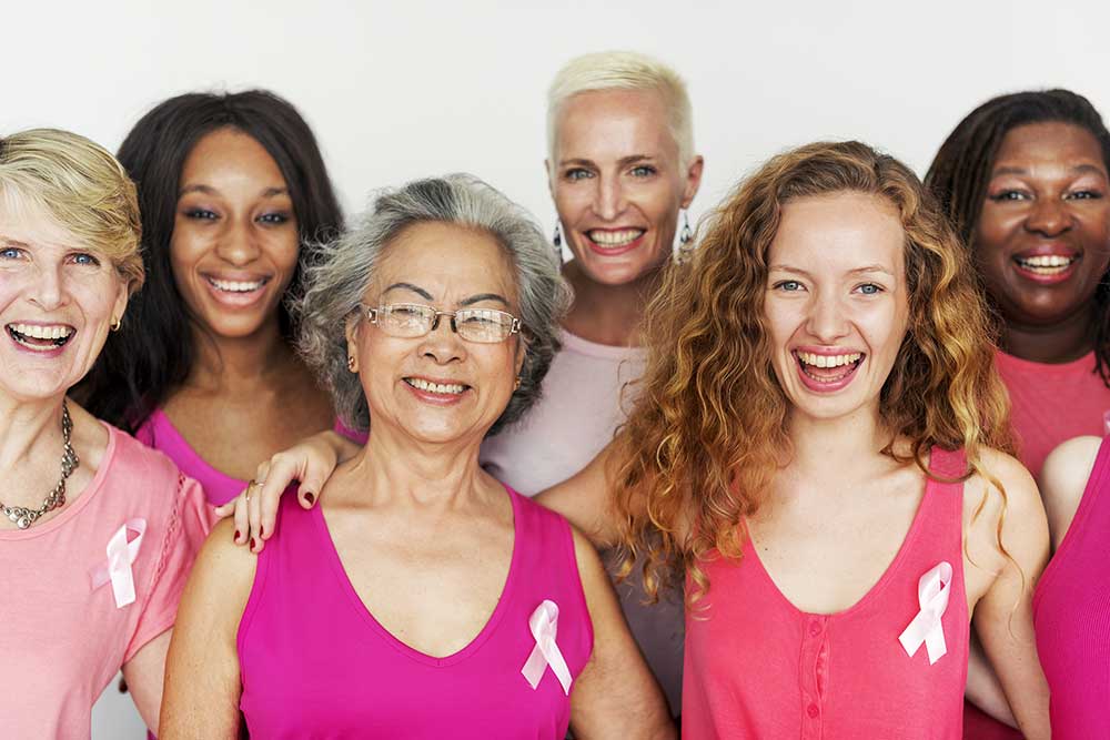 A group of women wearing breast cancer awareness ribbons stand together and smile