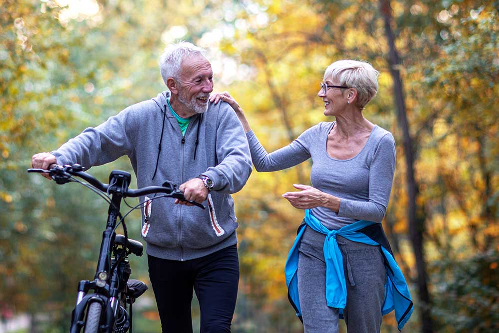 Mature couple woman and man with bicycle walking in the park and talk.