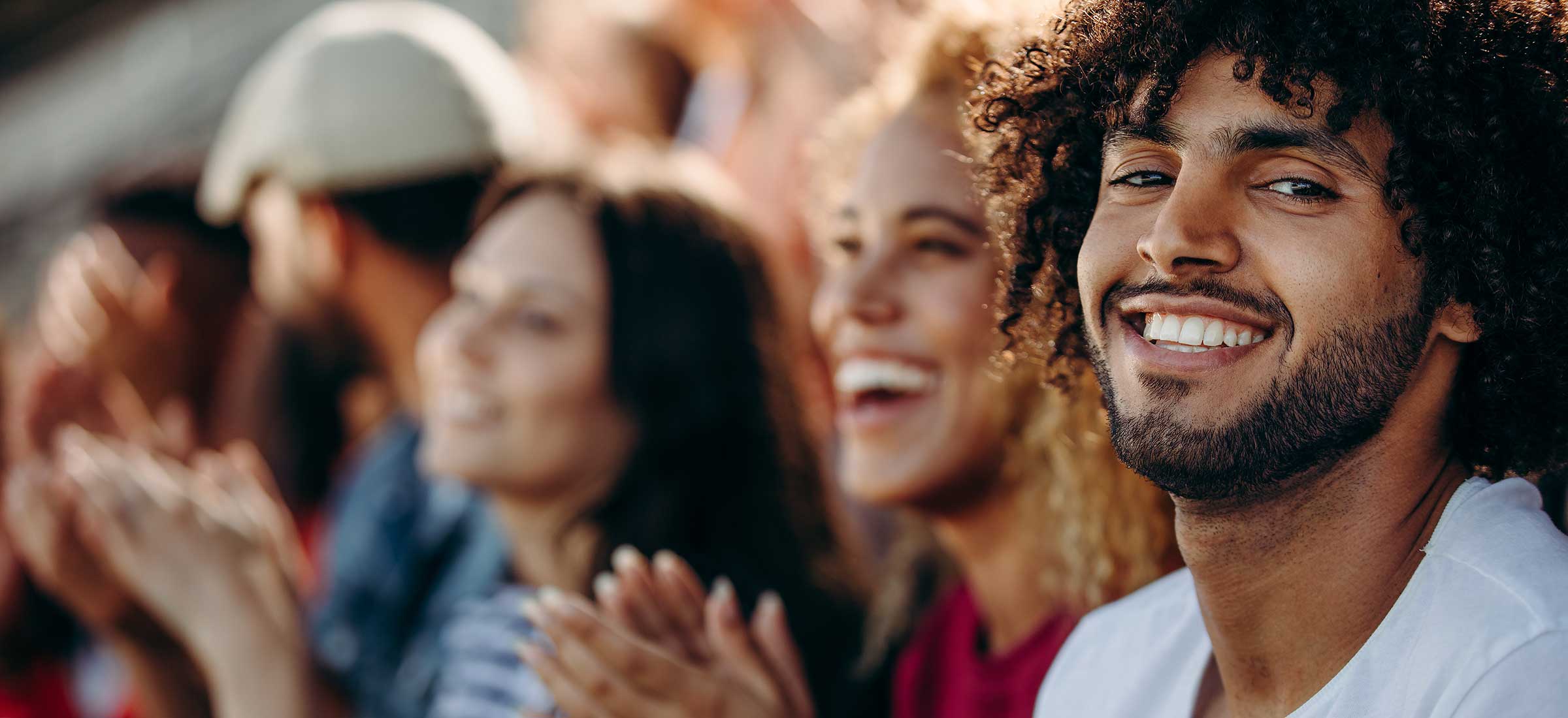 Man sitting with friends watching a soccer match and applauding at stadium.