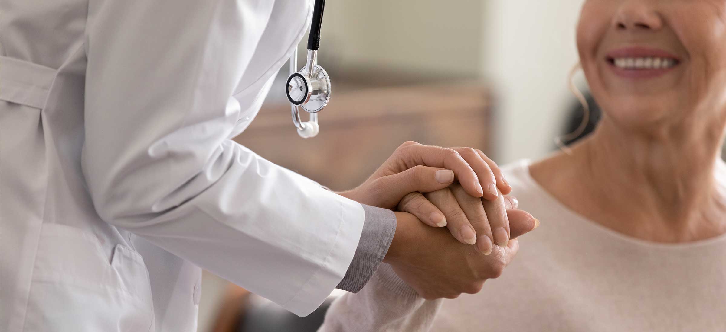 Close up shot of young female physician leaning forward to smiling elderly lady patient holding her hand in palms.