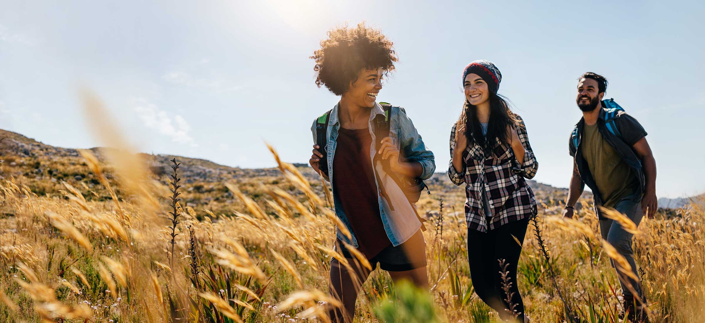 A group of three friends hike on a sunny day in the countryside.